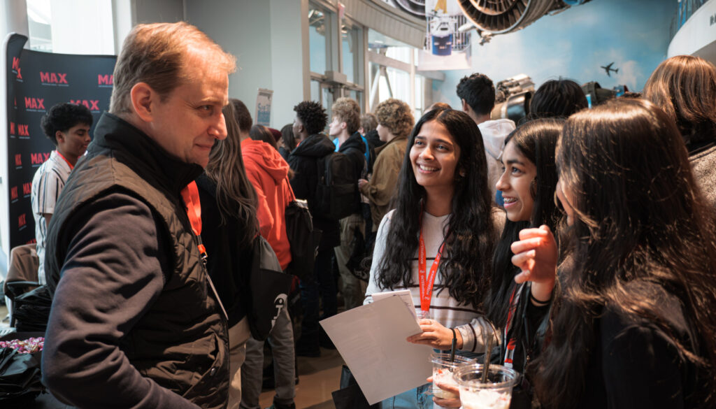 Photo of Students collaborating at TechOlympics, laptops open, mentors observing.